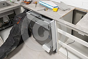 Appliance technician working under a kitchen sink installing a dishwasher
