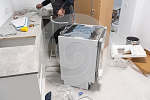 Appliance technician working under a kitchen sink installing a dishwasher