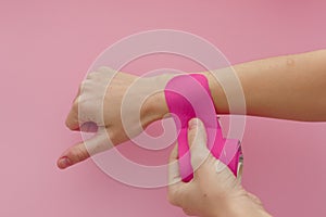 Appling a kinesio tape to hand  on pink background. Physiotherapy tape for wrist pain, aches and tension