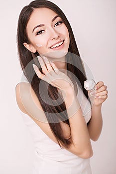 Applying cosmetic cream. A beautiful young woman applying face moisturizer. Scine care of the face and hands