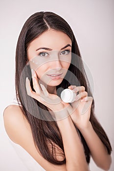 Applying cosmetic cream. A beautiful young woman applying face moisturizer. Scine care of the face and hands