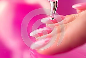 Applying cuticle oil in pipette, on fingers, manicure salon. Nail care, polish, pink shellac UV gel, varnish, manicure process