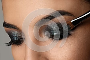 Applying dark eye shadow with brush onto woman`s face, closeup. Beautiful evening makeup