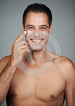 Applying his warpaint- its a battle against aging. Studio shot of a handsome mature man applying moisturizer to his skin