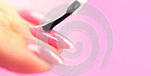 Applying nail polish on woman nails pink shellac UV gel, varnish, manicure process concept in beauty salon photo