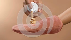 Applying self-tanner mousse to a rose massage glove. Ready to use. High quality studio photo image beige background.