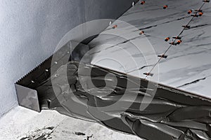 Applying tile glue to the floor using a tiling comb.