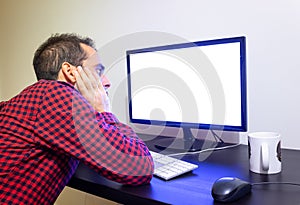 Apprehensive Man Stares at Office Computer on Wooden Black Desk Mockup. Dotted Red Shirt, LCD Screen, Keyboard, Mouse, White Mug.
