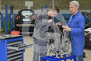 Apprentice mechanic in auto shop working on car engine