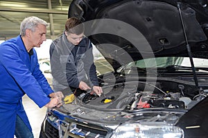 Apprentice mechanic in auto shop working on car engine