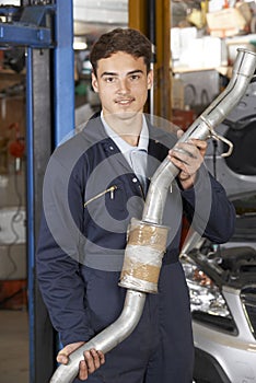 Apprentice Mechanic Holding Exhaust Pipe In Auto Repair Shop