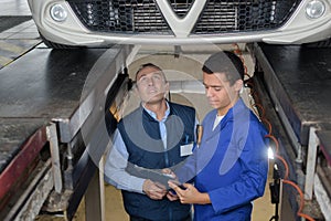 Apprentice mechanic repairing car monitored by mentor