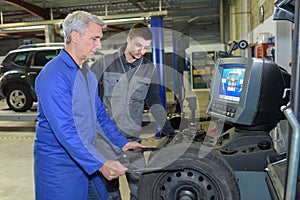 Apprentice mechanic and teacher retreading wheel in automotive workshop
