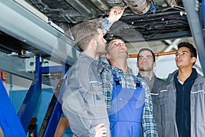 apprentice mechanics looking at car raised on hydraulic lift