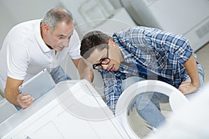 Apprentice repairman with instructor repairing washing machine