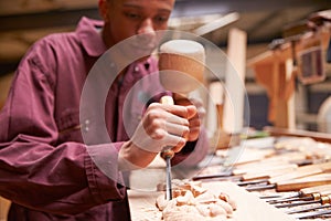 Apprentice Using Chisel To Carve Wood In Workshop