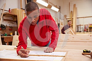 Apprentice Working With Plans In Carpentry Workshop