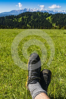 Approach shoes on the feet of a tourist resting during a trip on green grass in a clearing with a view of the mountain ridge