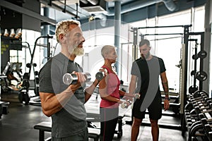 Approachable trainer supporting elderly couple while gym workout