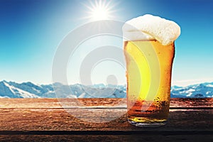 apres ski - cold beer glass on the table with sunny winter mountains landscape at ski resort