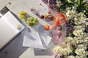 Apricot and cherry juice, apricots, cherries and grapes on a sunny table next to a notebook and laptop, copy space, top view.