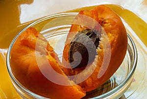 Apricot fruit is broken into lobes with a bone lying in a glass saucer