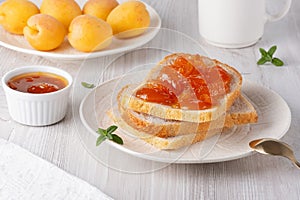 Apricot jam on bread in a white plate and a jar of apricot jam