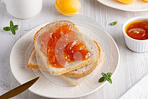 Apricot jam on bread in a white plate and a jar of apricot jam