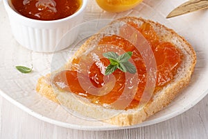 Apricot jam on bread in a white plate and a jar of apricot jam