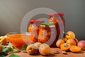 Apricot jam in a plate and glass jars. Fresh apricots fruit with leaves on table background