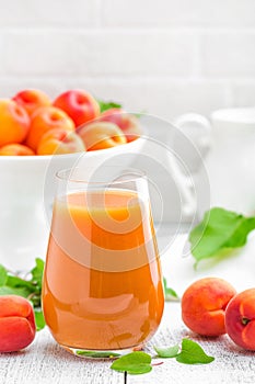 Apricot juice and fresh fruits with leaves on white wooden table