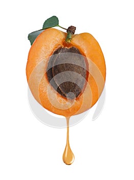 Apricot kernel oil dripping from fresh fruit half on background