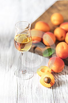 Apricot liqueur in shot glass and fresh apricots on a light wooden table