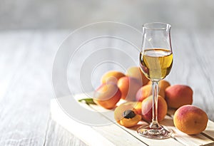 Apricot liqueur in shot glass and fresh apricots on a light wooden table