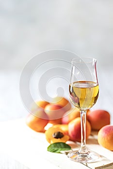 Apricot liqueur in shot glass and fresh apricots on a light wooden table