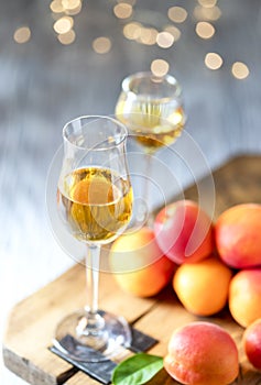 Apricot liqueur in shot glass and fresh apricots on a light wooden table in holiday colorful bokeh