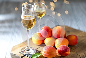 Apricot liqueur in shot glass and fresh apricots on a light wooden table in holiday colorful bokeh