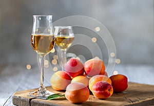 Apricot liqueur in shot glass and fresh apricots on a light wooden table in holiday colorful bokeh