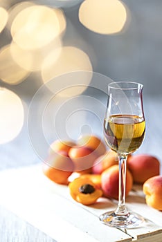 Apricot liqueur in shot glass and fresh apricots on a light wooden table in holiday colorful bokeh