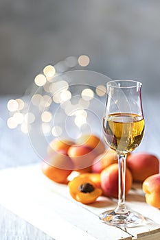 Apricot liqueur in shot glass and fresh apricots on a light wooden table in holiday colorful bokeh