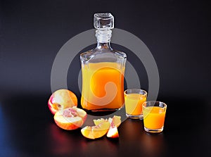 Apricot liqueur in two glasses and a bottle, ripe cut fruits next to it on a black background