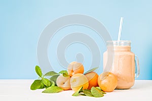 Apricot milkshake decorated with fresh apricots and green leaves on white and blue background