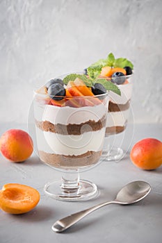 Apricot trifle, chocolate biscuit, layered dessert with fresh berry and gentle cream cheese on grey background. Selective focus