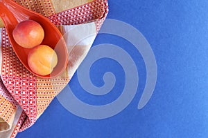 Apricots, orange saucer, checkered kitchen orange towel on a blue background with space for text. Apricots and space for text.