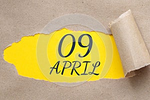April 09. 09th day of the month, calendar date. Hole in paper with edges torn off. Yellow background is visible through