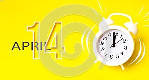 April 14th. Day 14 of month, Calendar date. White alarm clock  with calendar day on yellow background. Minimalistic concept of