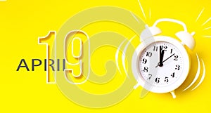 April 19th. Day 19 of month, Calendar date. White alarm clock  with calendar day on yellow background. Minimalistic concept of