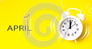 April 1nd. Day 1 of month, Calendar date. White alarm clock  with calendar day on yellow background. Minimalistic concept of time