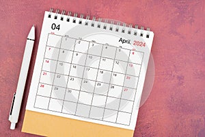 April 2024 desk calendar and pen on red background