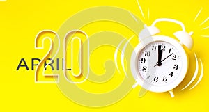 April 20th. Day 20 of month, Calendar date. White alarm clock  with calendar day on yellow background. Minimalistic concept of